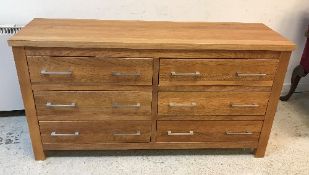 A modern teak bank of six drawers with polished metal handles, raised on stile supports,