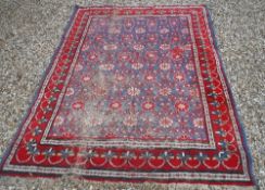 A Persian carpet, the central panel set with all-over flower head motifs on a blue ground,