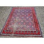 A Persian carpet, the central panel set with all-over flower head motifs on a blue ground,