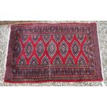A Bokhara rug, the central panel set with repeating medallions on a red ground,