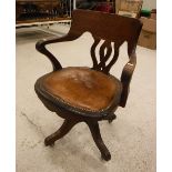 An office swivel elbow chair with studded brown leather seat on quadruped base and castors,