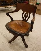 An office swivel elbow chair with studded brown leather seat on quadruped base and castors,