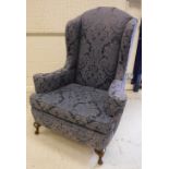 An early 20th Century upholstered wing back scroll arm chair in the Georgian style raised on