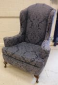 An early 20th Century upholstered wing back scroll arm chair in the Georgian style raised on