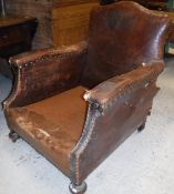 A pair of early 20th Century studded brown leather covered armchairs,