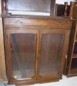 A Victorian oak bookcase cabinet with two glazed doors enclosing adjustable shelving over a single