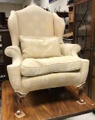 A modern upholstered wing back scroll armchair on shell carved cabriole legs to pad feet in the