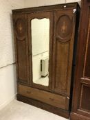 An Edwardian mahogany and inlaid single mirror door wardrobe with drawer below raised on a plinth