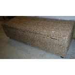 A modern seagrass covered ottoman on stained wood square tapered legs,