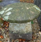 A natural stone staddle stone with circular top on a tapered base,