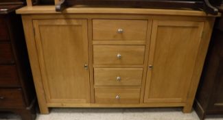 A modern light oak sideboard with four central drawers flanked by two cupboard doors,