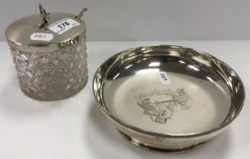 A shallow silver bowl of plain form with engraved decoration to centre depicting a stork at a door