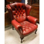 A buttoned red leather upholstered wing back scroll arm chair in the George III taste,