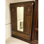 An Edwardian mahogany and inlaid single mirror door wardrobe with drawer below raised on a plinth