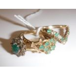 Three various 9 carat gold and emerald dress rings, one of flower head design,
