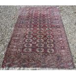 A Bokhara rug, the central panel set with repeating elephant foot medallions on a red ground,