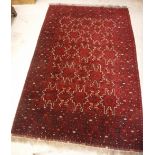 A Persian rug with repeating stylized leaf shape medallions on a red ground within a similarly