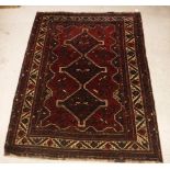 A Persian rug with three repeating lozenge medallions on a red ground, within a cream ground border,