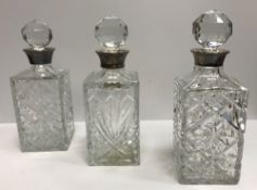 Three modern cut glass decanters with silver rims, various dates and makers and matching stoppers,