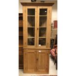 A pine freestanding corner cupboard with two glazed doors enclosing three shelves over two panel