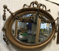 A circa 1900 carved giltwood and gesso framed wall mirror of oval form with floral swag and ribbon