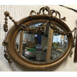 A circa 1900 carved giltwood and gesso framed wall mirror of oval form with floral swag and ribbon