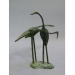A reproduction bronze figure of two interlaced cranes standing on a rustic shaped oval base, 24cm