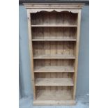 A reproduction pine bookcase with flared cornice, shaped frieze and adjustable shelves, skirted