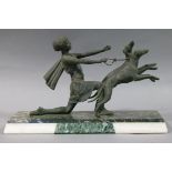 An Art Deco patinated white metal figure of a young woman holding a pair of leaping hounds,