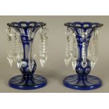 A PAIR OF VICTORIAN BLUE CASED AND CLEAR GLASS LUSTRES, the knopped stem having a flared neck with