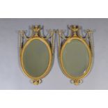 A PAIR OF EDWARD VII GILT WALL MIRRORS the oval bevelled plate within a beaded frame with urn and