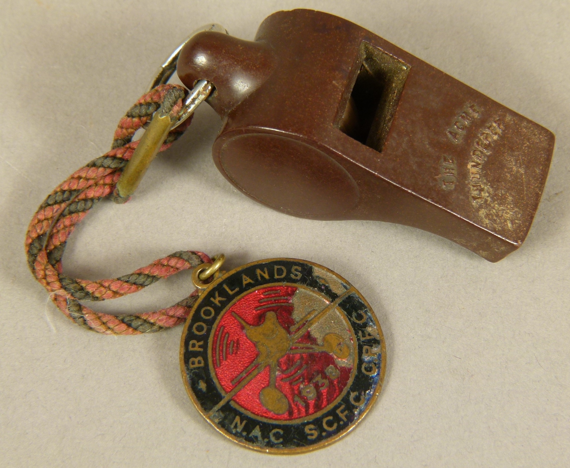 A BROOKLANDS BRASS AND ENAMEL FLYING MEDALLION, circular, worked with a plane on a red enamel