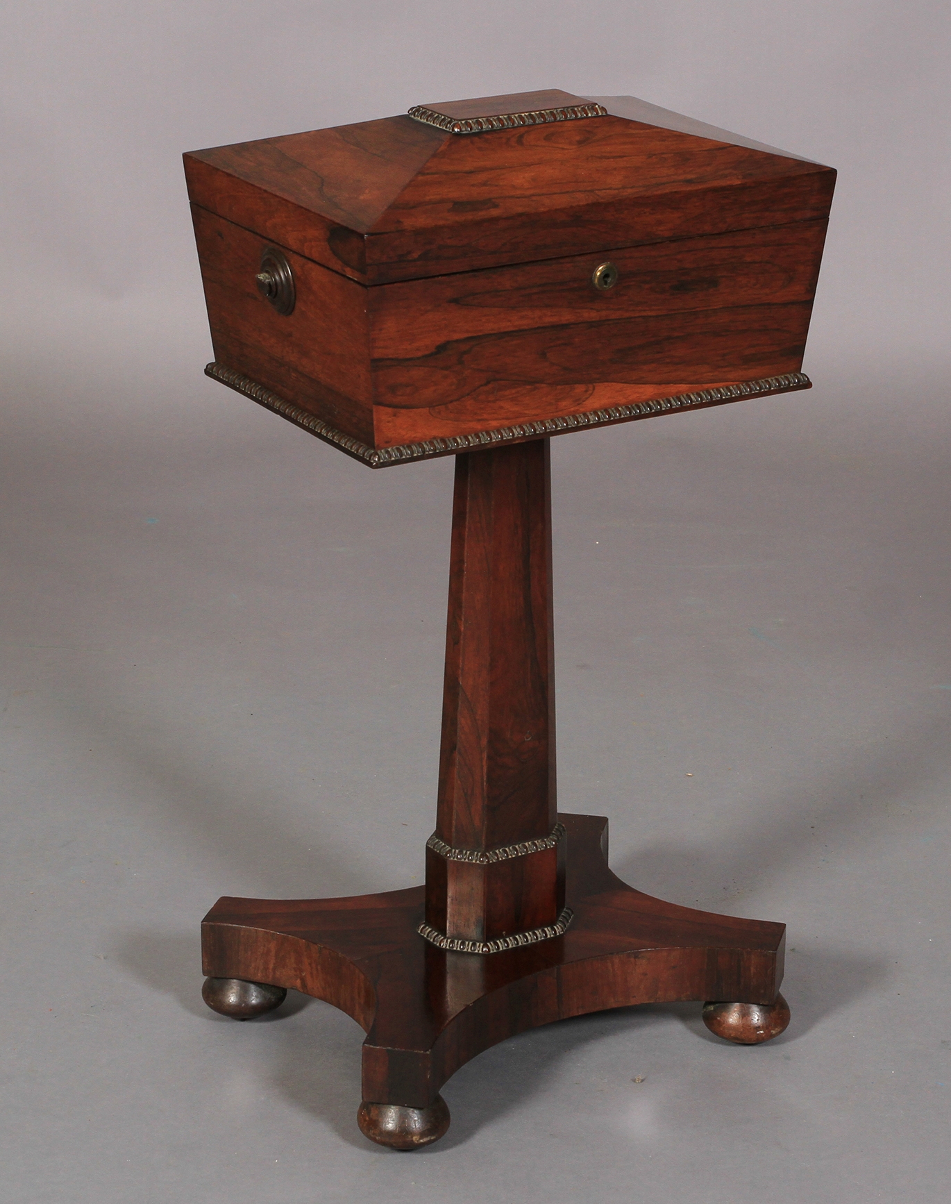 A REGENCY ROSEWOOD VENEERED TEAPOY of conventional form, the sarcophagus shaped top with reel