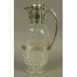 A LATE VICTORIAN SILVER MOUNTED CRYSTAL CLARET JUG of oval flattened form, the semi-domed cover with