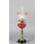 A VICTORIAN BRASS FLUTED COLUMN OIL LAMP with circular black pottery base, moulded cranberry