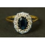 A SAPPHIRE AND DIAMOND CLUSTER RING, the oval faceted sapphire claw set within a surround of