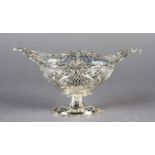 A SILVER PEDESTAL BASKET, pierced cast and chased, the oval body with foliate clasped border and