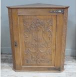 An oak corner cupboard, the panelled door carved with pomegranate flowers, buds and scrolling