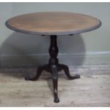 A George III style mahogany tripod table, the circular top with foliate carved lip above baluster