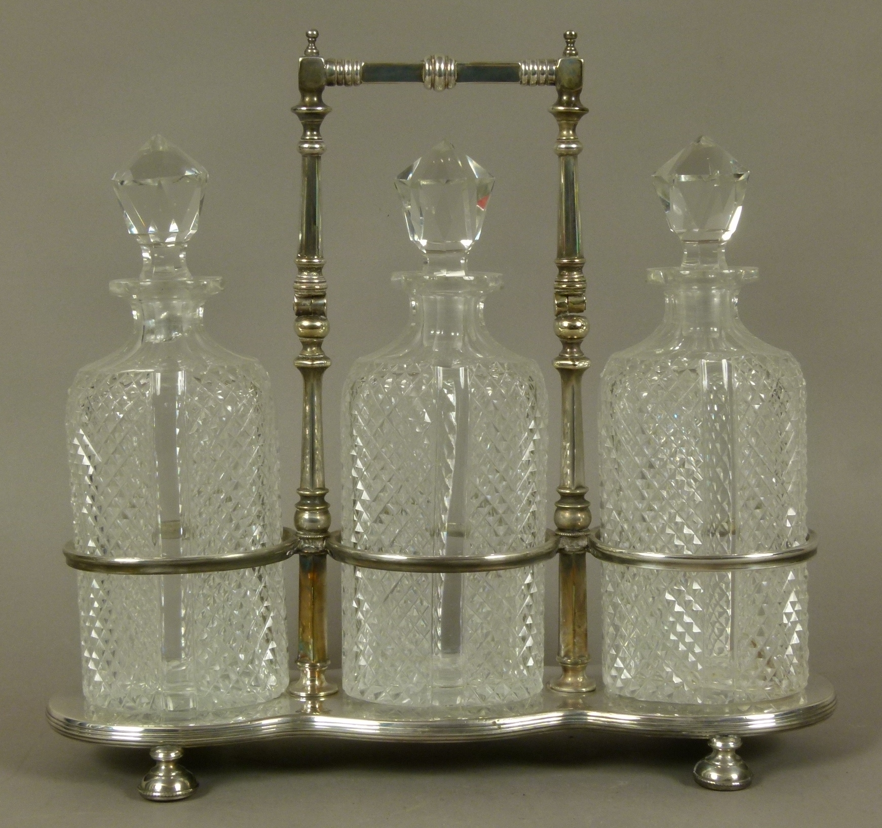 A late Victorian/Edwardian VII silver plated triple decanter stand and three diamond cut glass