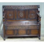 An oak monks bench, the folding top carved to the underside with trailing foliage and three