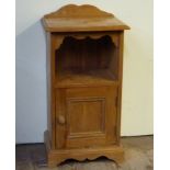 A reproduction pine bedside cupboard with shaped back, open shelf, panelled cupboard and shaped
