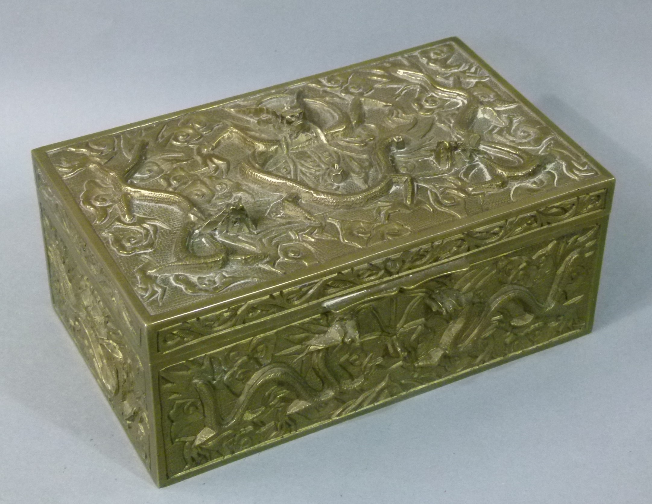 A 20th century Chinese brass box cast in relief with dragons amongst clouds to each panel