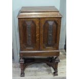 An oak cabinet having a lift up top with shallow well above two canted panelled doors the interior