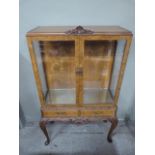 A reproduction burr walnut veneer display cabinet with shell carved cresting, bevelled glazed