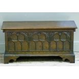 A reproduction oak kist having a hinged lid over a triple Gothic style arch carved front on shaped