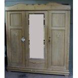 A 1920s pine three door wardrobe having a shaped pediment above a mirrored door to the centre