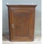 A George III oak hanging corner cupboard with dentil moulded cornice the panelled door centred on
