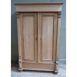 A pine wardrobe having a moulded cornice above a plain frieze, two indented panel doors and deep