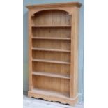 A pine open bookcase with moulded cornice and arched frieze with six shelves and shaped apron